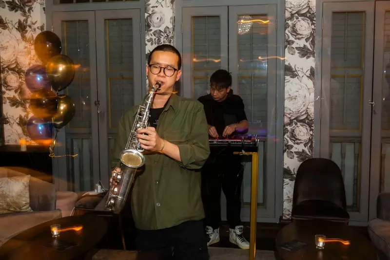 Saxophonist in an olive shirt playing in front of the DJ booth at a party