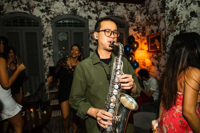 Saxophonist playing a silver alto sax among dancing guests at an evening party