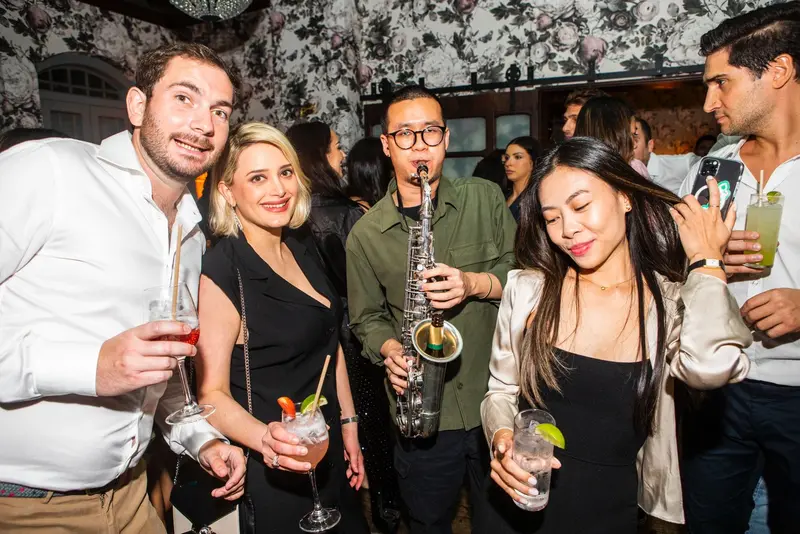 Saxophonist playing among smiling guests holding drinks at a party