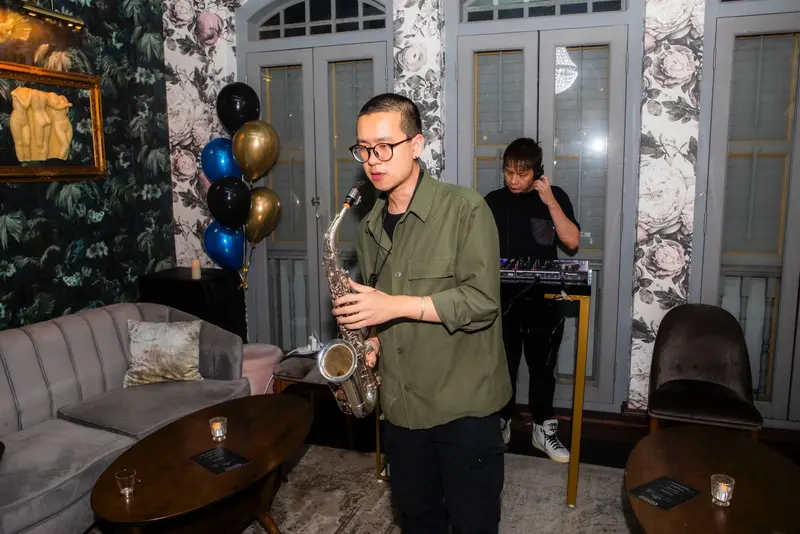 Saxophonist playing next to a DJ in a lounge decorated with blue and gold balloons